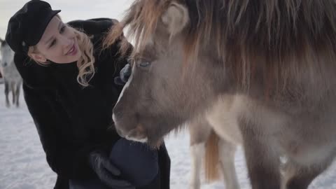 Young smiling woman strokes muzzle of adorable small pony at a ranch close up