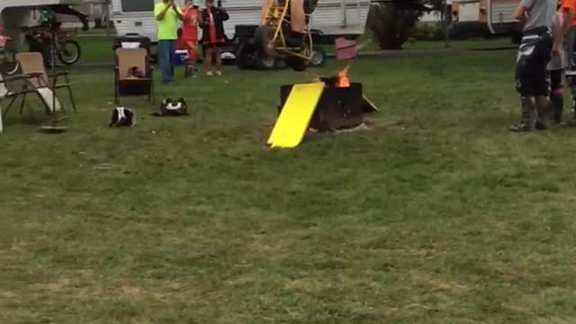 Guy in orange shirt does ramp jump over small fire on mini motorcycle