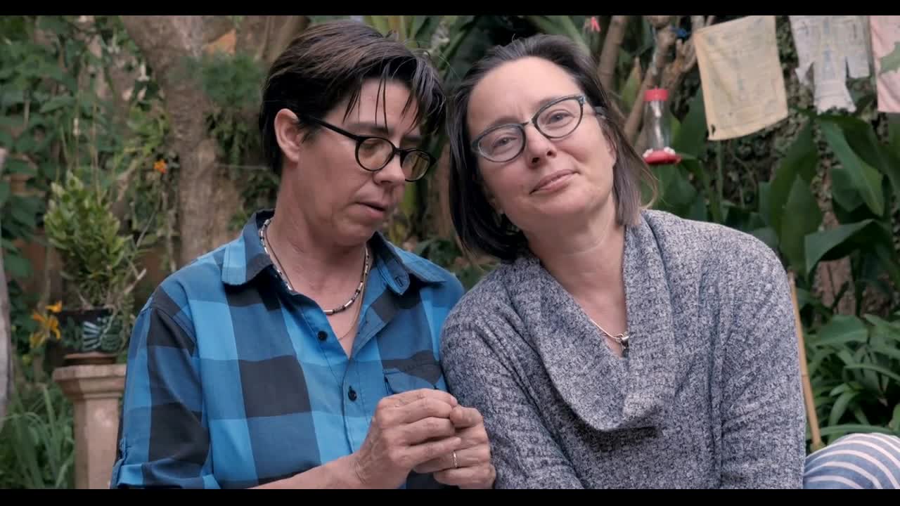 Two women sitting next to each other while their dog looks at them waiting for a command