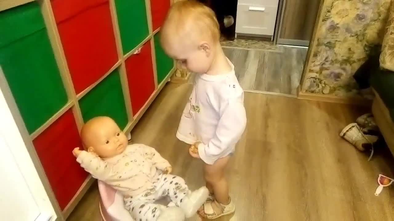 The baby is waiting for the doll to do something on the baby potty.