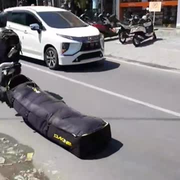 Guy dragging black bag on floor ground street while riding motorcycle with helmet