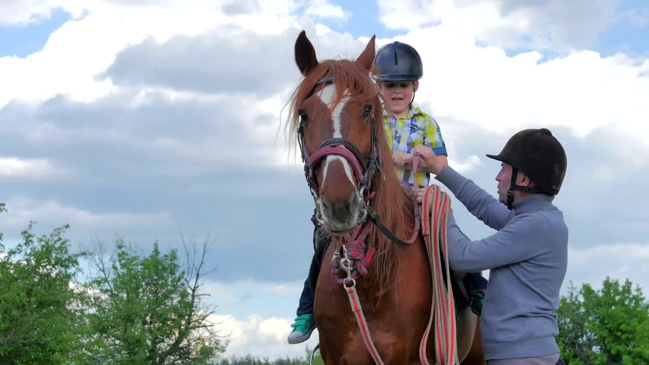 Father teaching little son to sit on horse and holding a rein in hands