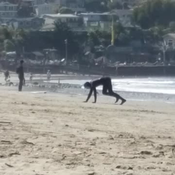 Man in black wetsuit crawling towards beach