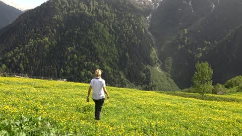 Blonde woman walking in a flower field in the mountain