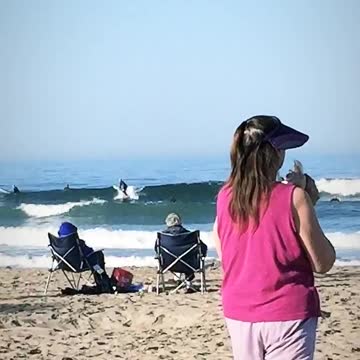 Pink shirt woman blows conch shell on beach