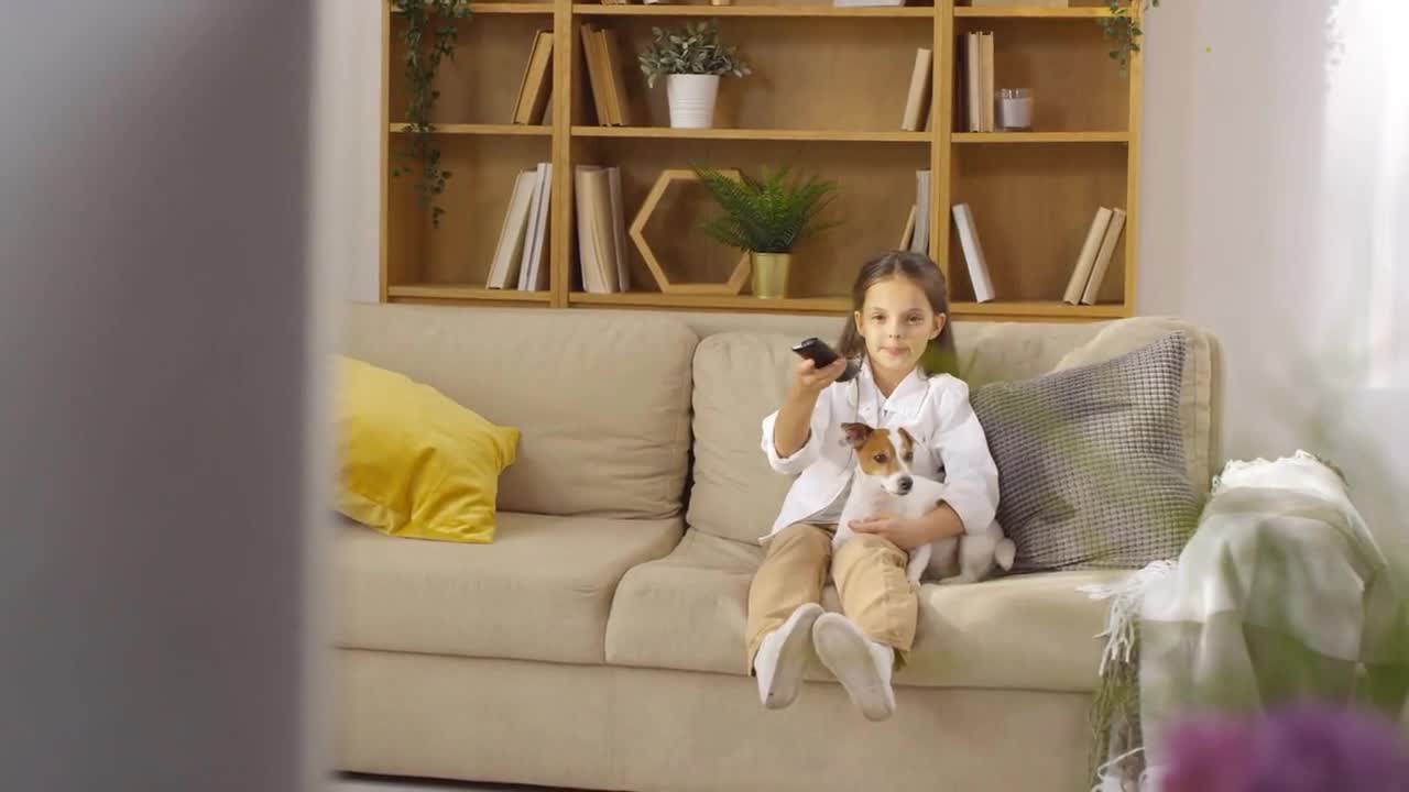 old girl sitting on sofa in living room, cuddling with cute jack russel terrier dog