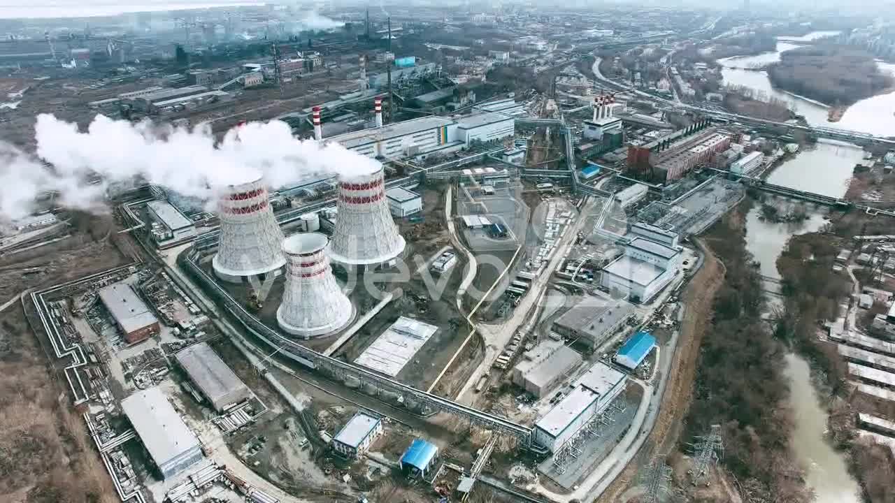 Aerial View Of Industrial Zone With Factories Expelling Smoke Around A Green Landscape