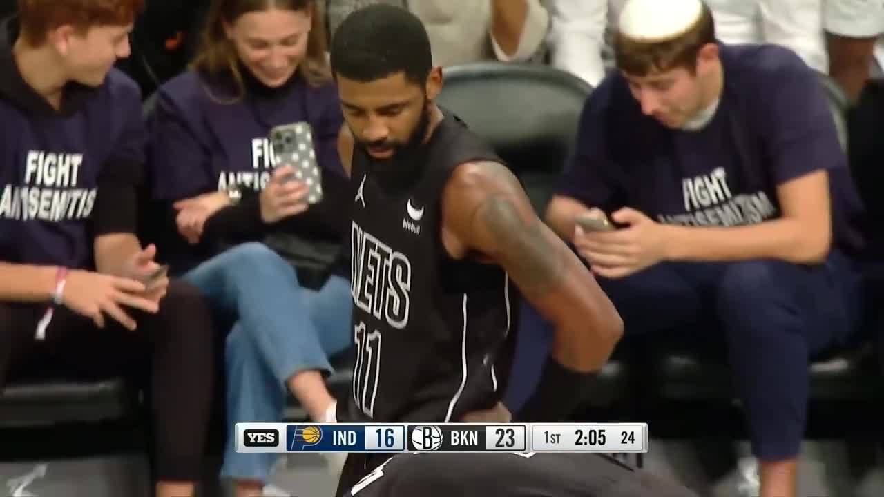 Kyrie Irving standing in front of courtside fans wearing "Fight Antisemitism" t-shirts