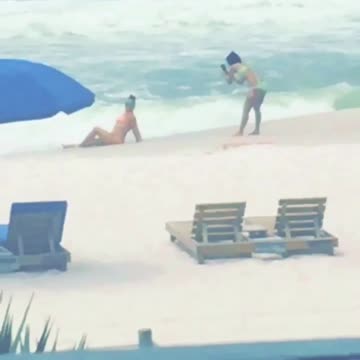 Two girls on beach taking pictures with narrator