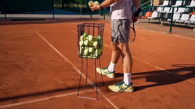 A Tennis Players Picking Balls From a Basket