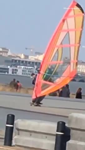 Guy skateboarding with an orange wind surfing kite