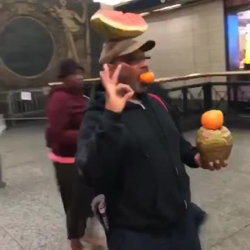 Guy balancing fruit with ok sign standing still subway