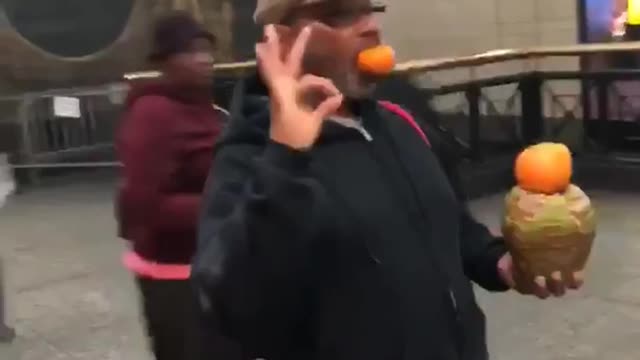 Guy balancing fruit with ok sign standing still subway