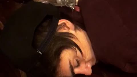 Friends pour water from coke bottle onto sleeping friends face on wooden bar