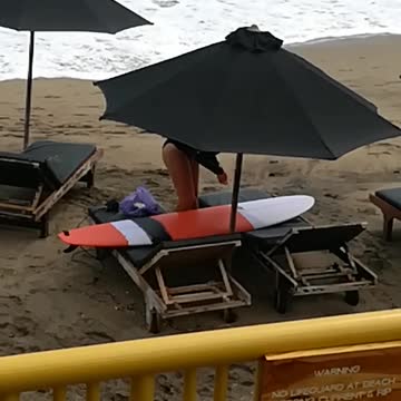 Music girl waxing orange surfboard under black umbrella