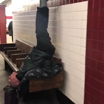 Man sits upside down on wooden bench with legs straight in the air