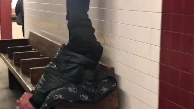 Man sits upside down on wooden bench with legs straight in the air