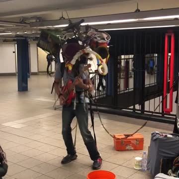 Man sings rudolph the rednose reindeer, plays guitar, other instruments on his back