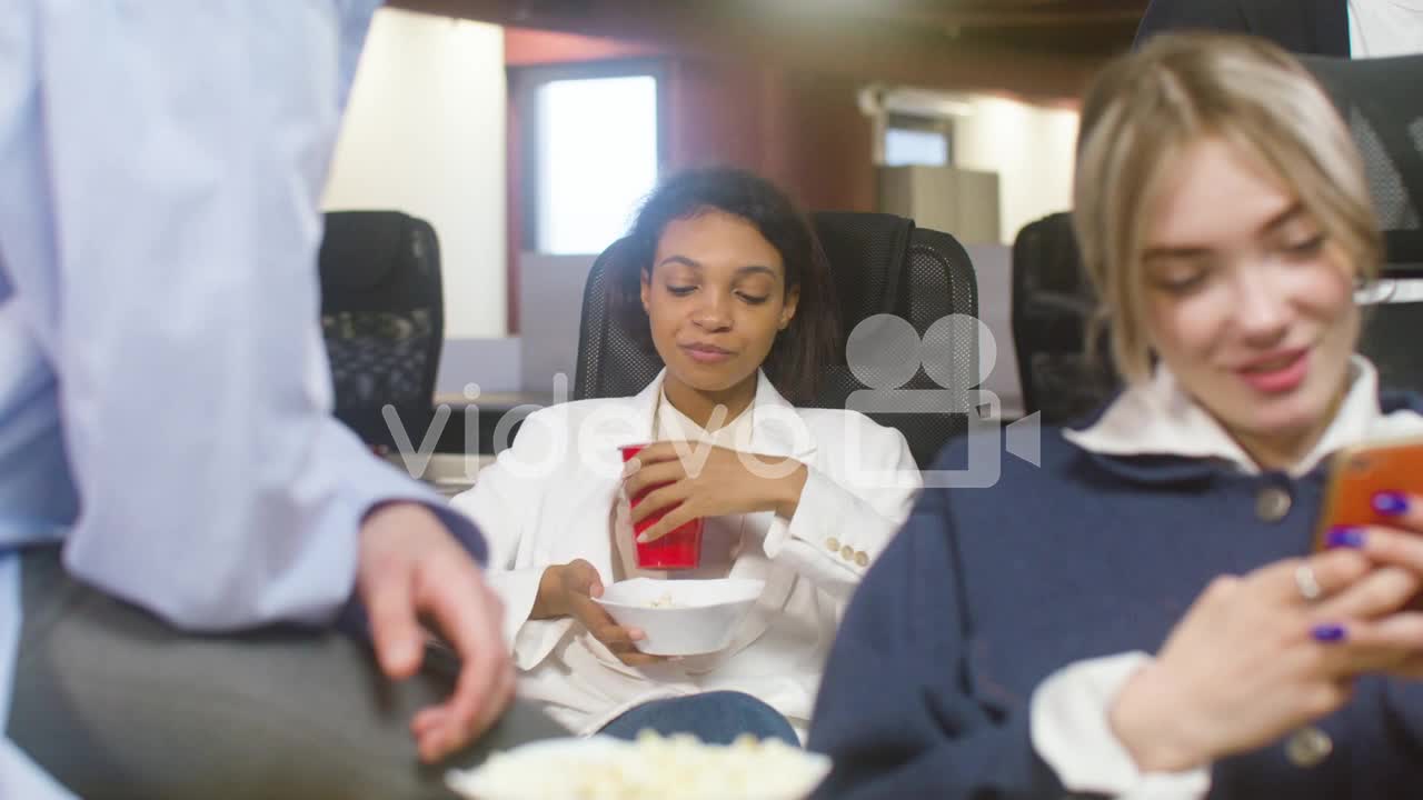 Girl Eating Popcorn And Drinking Soft Drink While Sitting At The Office With Her Colleagues During A