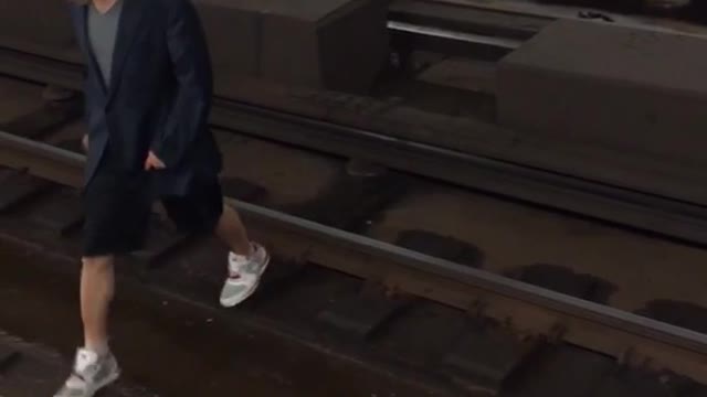 Guy black hoodie white shoes walks across tracks onto opposite platform