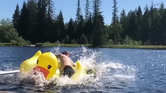 Man jumps on yellow duck inflatable toy in lake