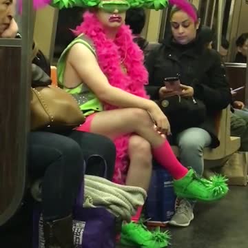 Man wears green and pink flower visor costume subway