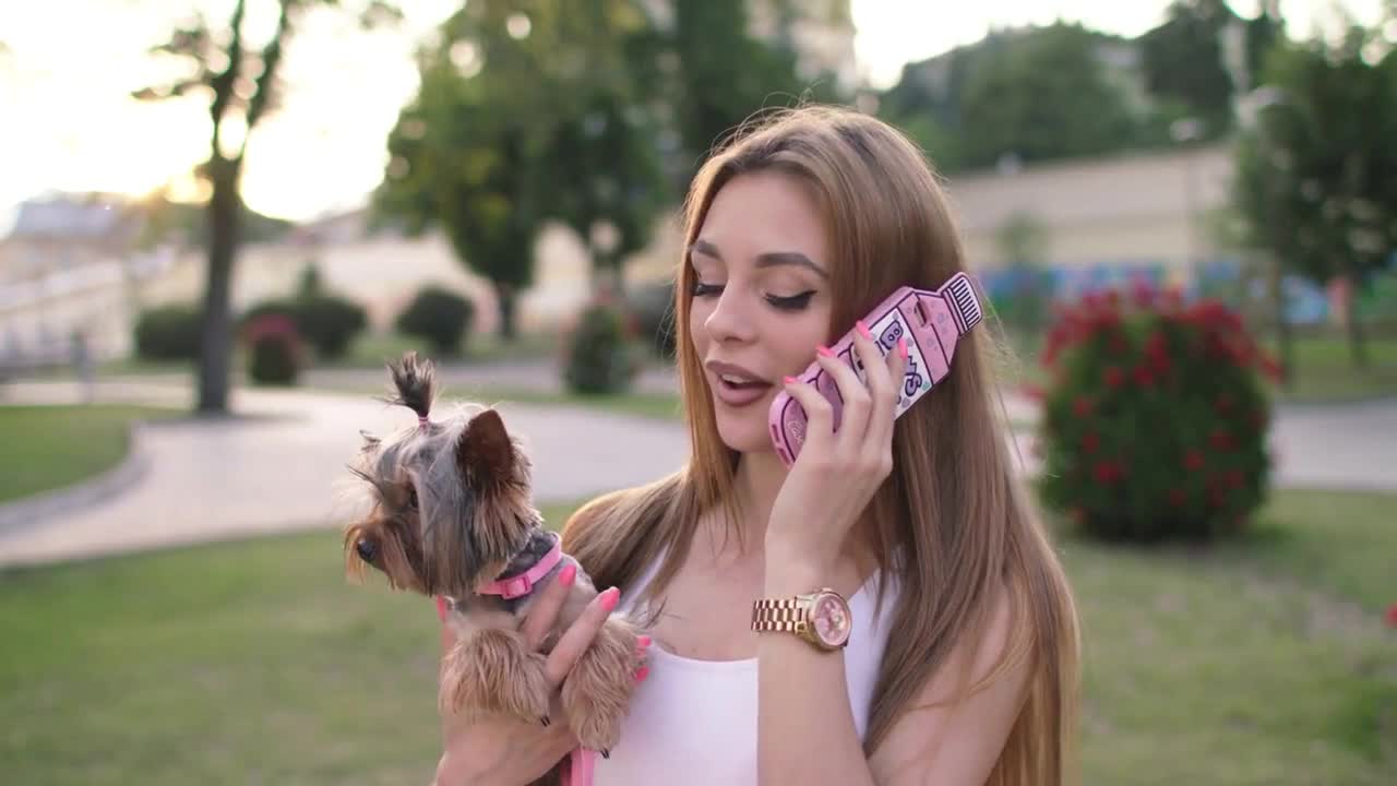 Beautiful Girl Walking With Her Small Dog In The City Park And Using Smartphone