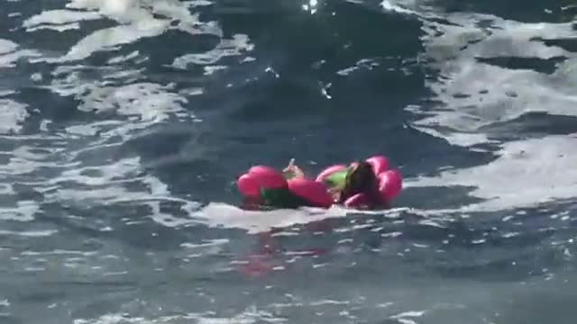 Woman in pink flower floatie crashes with waves