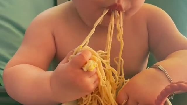 A baby girl eats spaghetti with passion